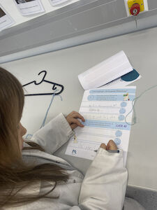 Ein Mädchen füllt im Forscherheft etwas über den klingenden Kleiderbügel aus.