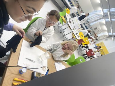 Zwei Kinder werden an der Lötstation von einer Frau unterstützt.