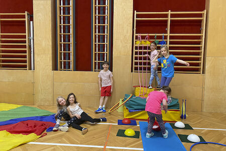 Eine Kindergruppe stellt ihre selbstgebaute Hütte bei den Sprossenwänden im Turnsaal vor.
