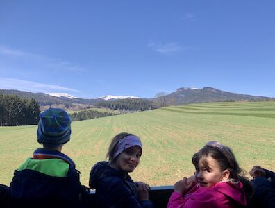 Zwei Mädchen werfen einen Blick in die Kamera währenddessen ein Bub von einer Aussichtsplattform in die Weite schaut.