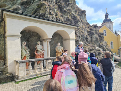Eine Kindergruppe steht vor einigen lebensgroßen Statuen und bekommt diese erklärt.