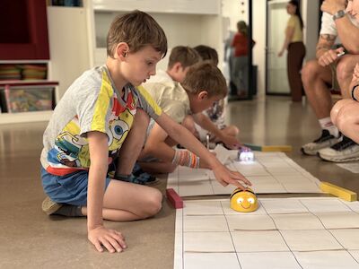 Kinder beim Programmieren von Bee-Bots am Boden auf einer Matte.