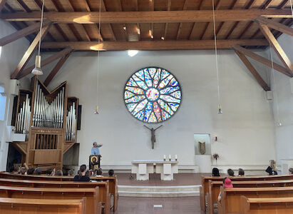 Innenansicht der Salvatorkirche, wo die Religionslehrerin am Altar den in den Kirchenbänken sitzenden Kindern über die Kirche etwas erzählt.