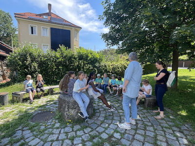 Kurze Besprechung mit den Kindern vor der Kirche im Schatten eines Baumes.