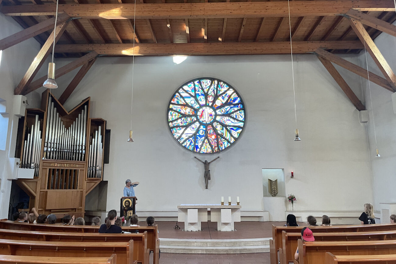 Innenansicht der Salvatorkirche, wo die Religionslehrerin am Altar den in den Kirchenbänken sitzenden Kindern über die Kirche etwas erzählt.