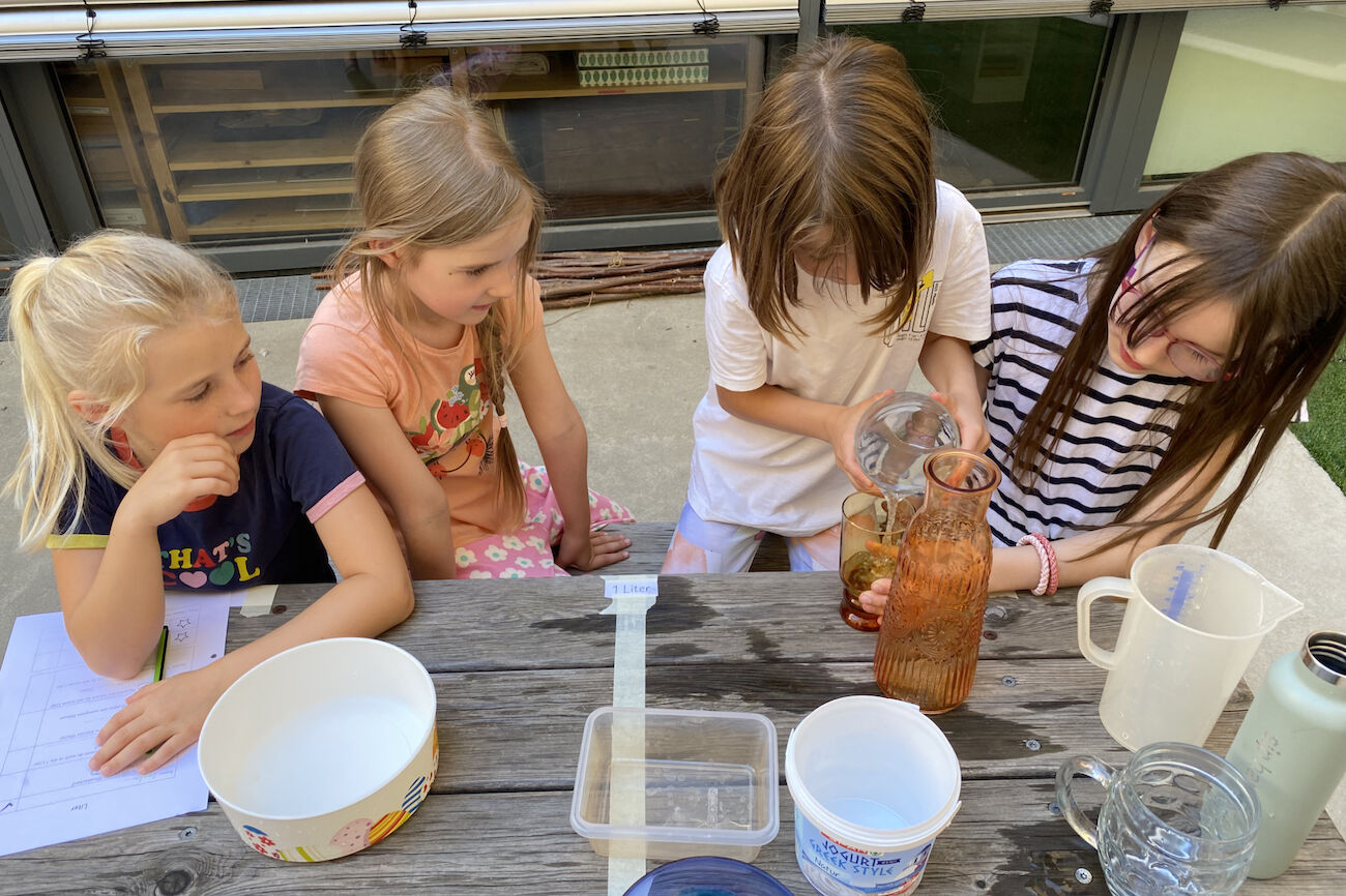 Eine Mädchengruppe versucht sich in Schütt- und Schätzübungen mit Wasser.