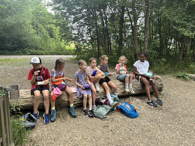 Beim Jausnen sitzen die Kinder auf einem dicken Baumstamm.