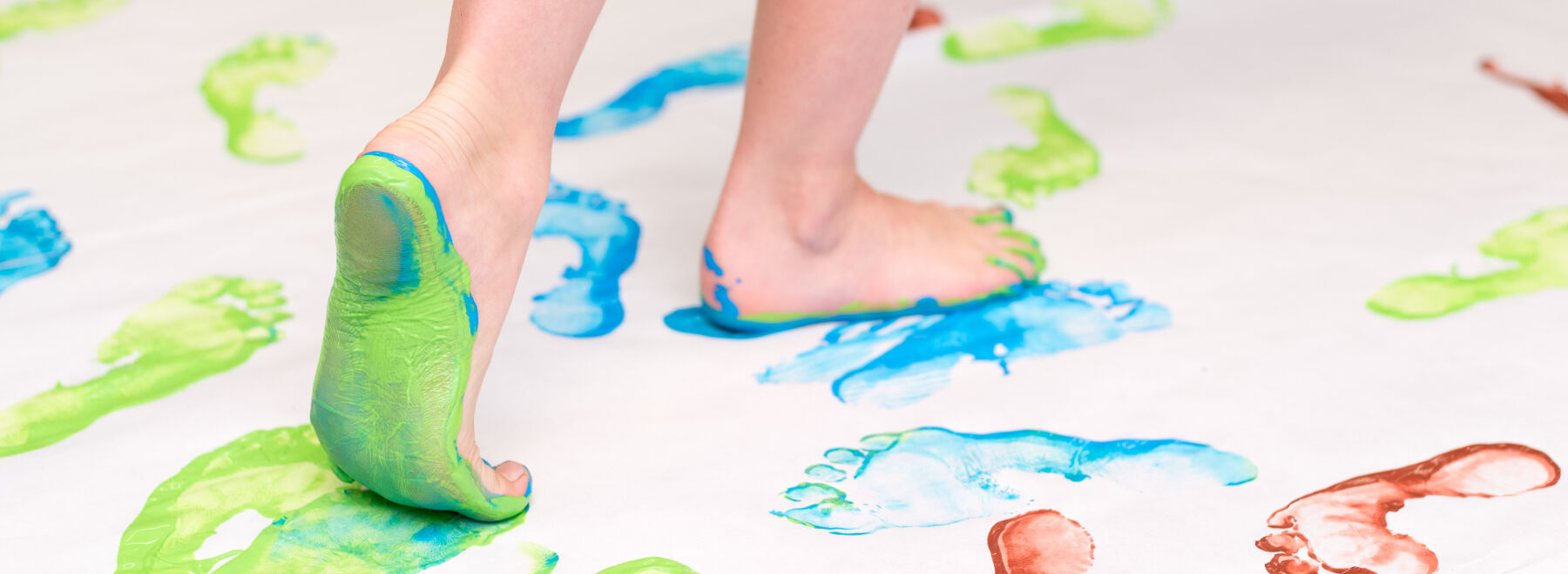 Mit Farbe angemalte Kinderfüße gehen über ein Plakat und hinterlassen Fußspuren.